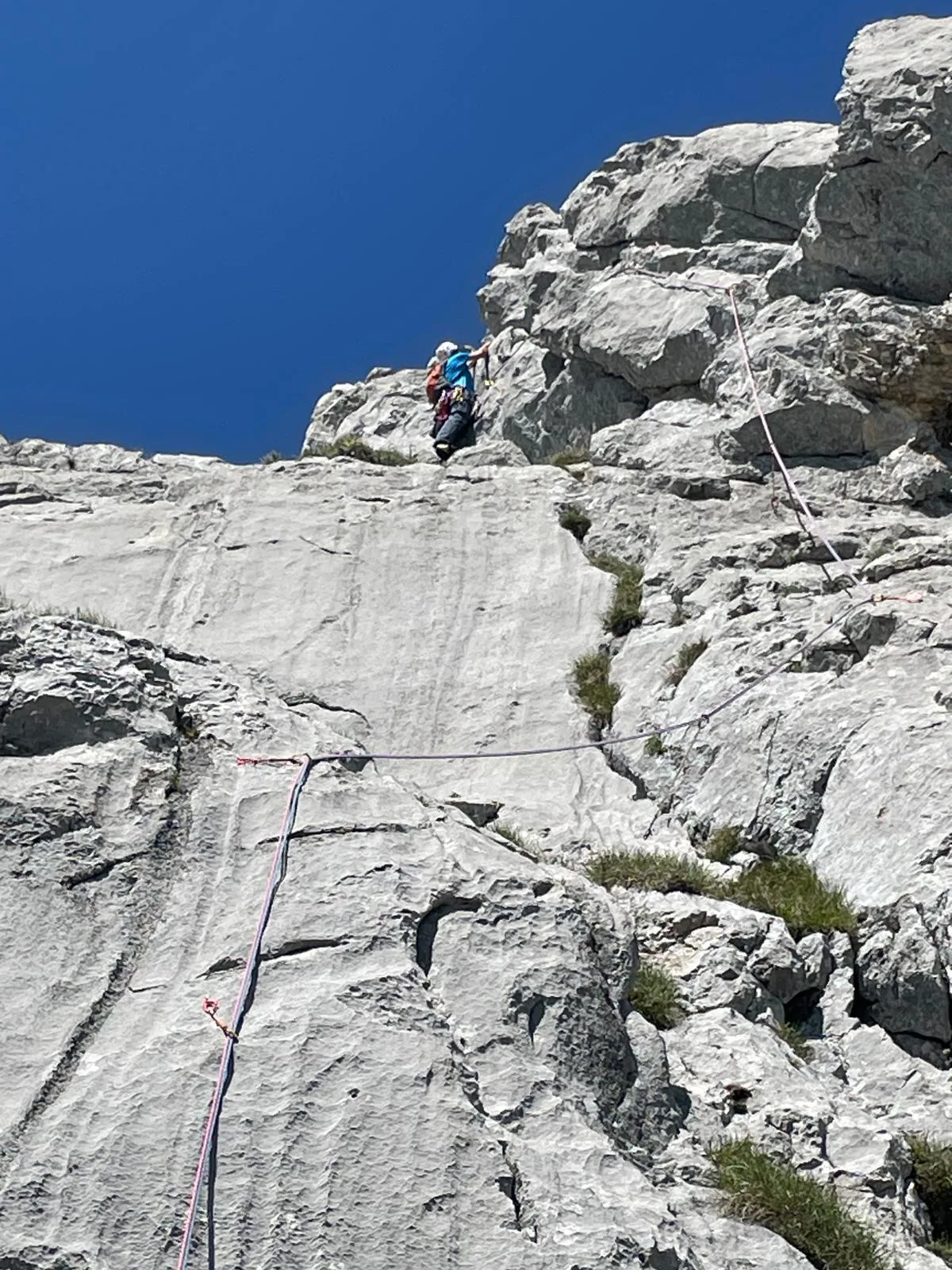 Grimpeur minuscule en haut d'une grande dalle calcaire grise sous un ciel bleu profond