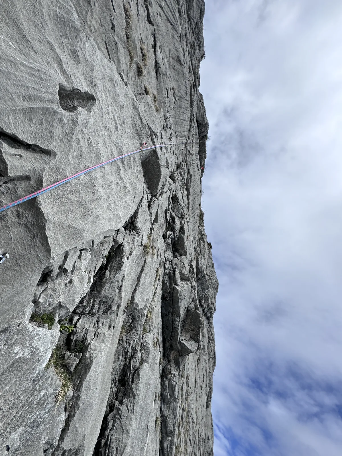 Paroi calcaire grise massive en contre-plongée avec une corde violette traversant le cadre