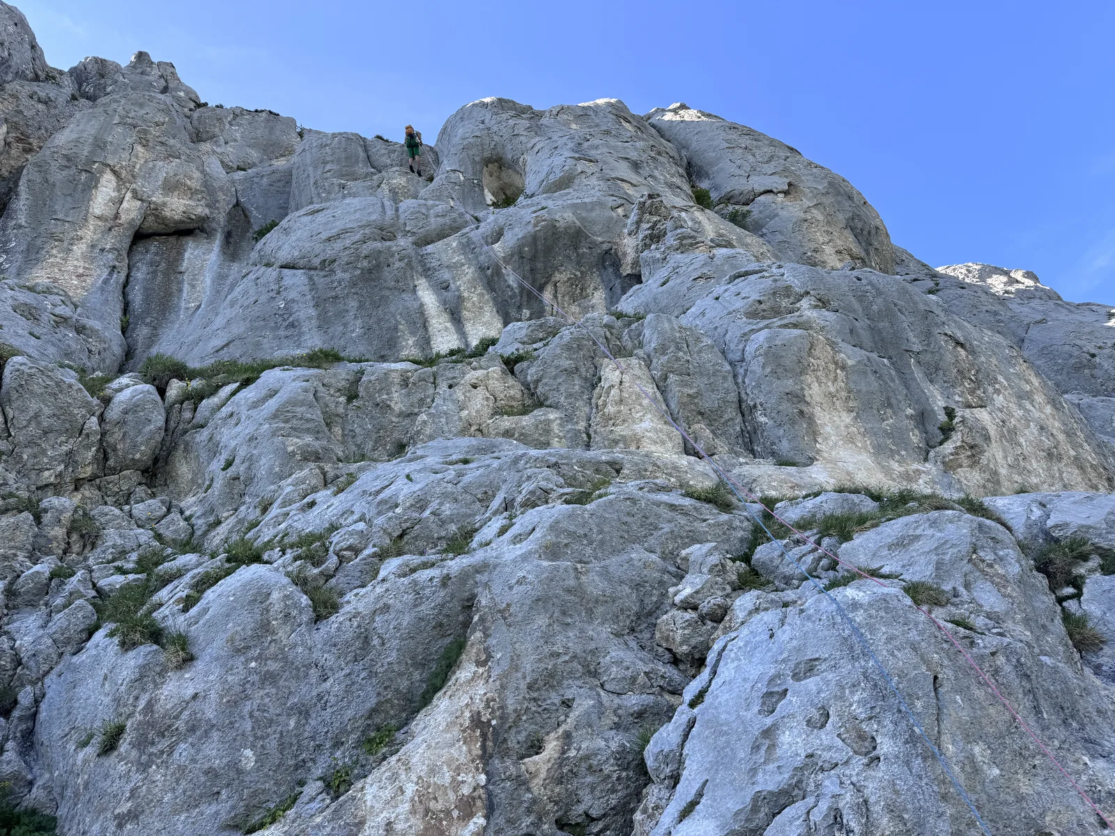 Paroi calcaire massive avec un grimpeur minuscule en haut, échelle humaine face à la paroi