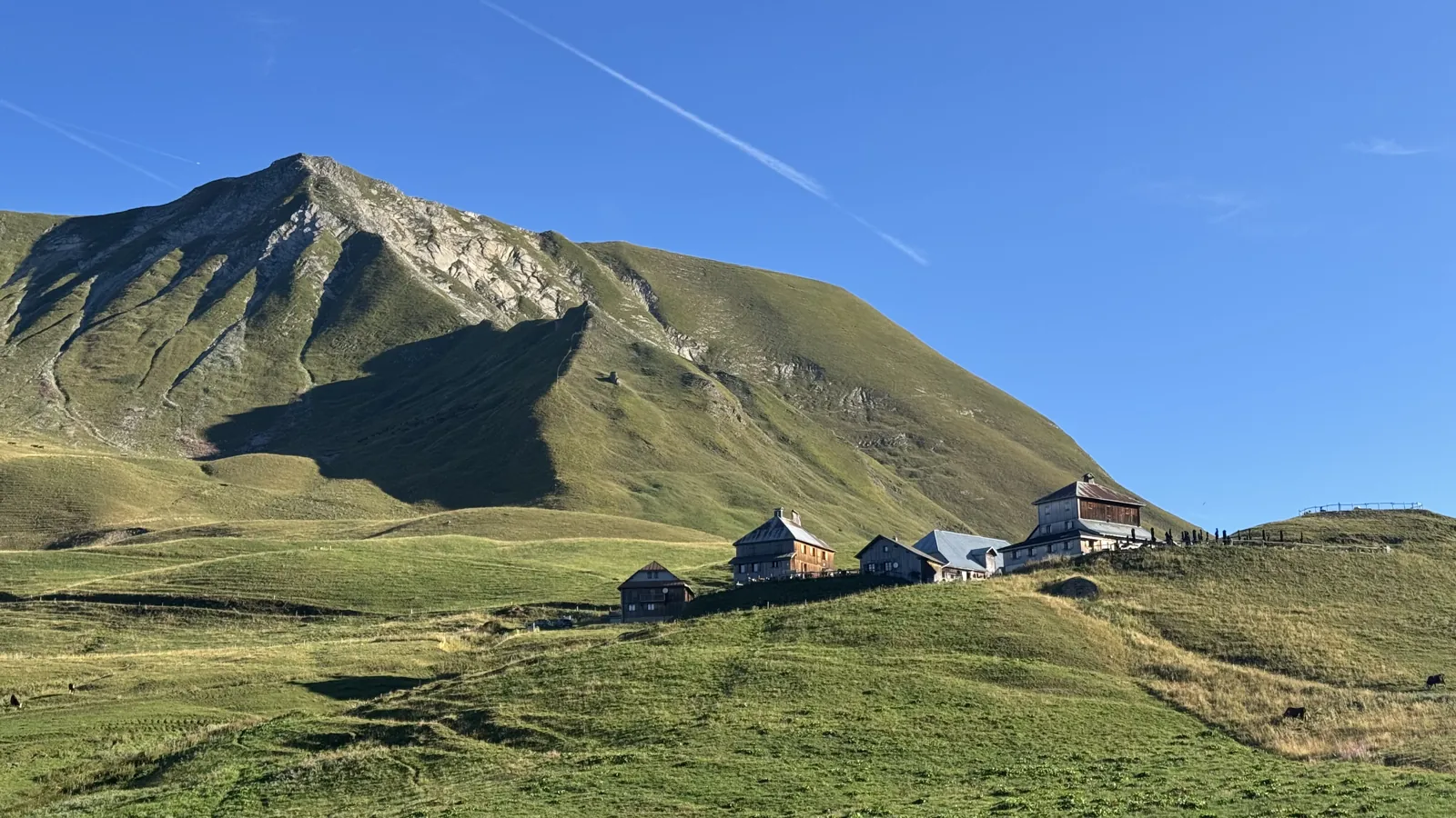 Alpage et chalets au pied d'un sommet herbeux, ciel bleu du matin