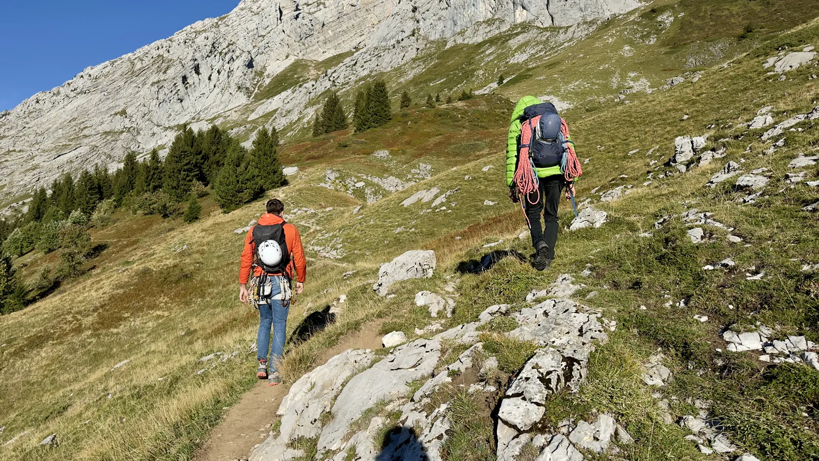 Cordée en marche d'approche sur un sentier d'alpage, sous les falaises calcaires