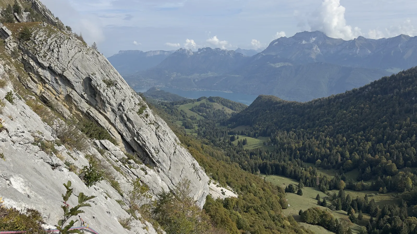 Vallée boisée et lac sous des nuages qui montent, vue depuis une dalle