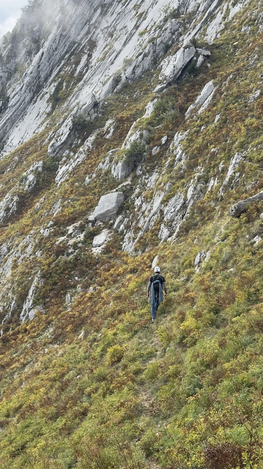 Grimpeur en traversée sur une pente herbeuse au pied de dalles calcaires
