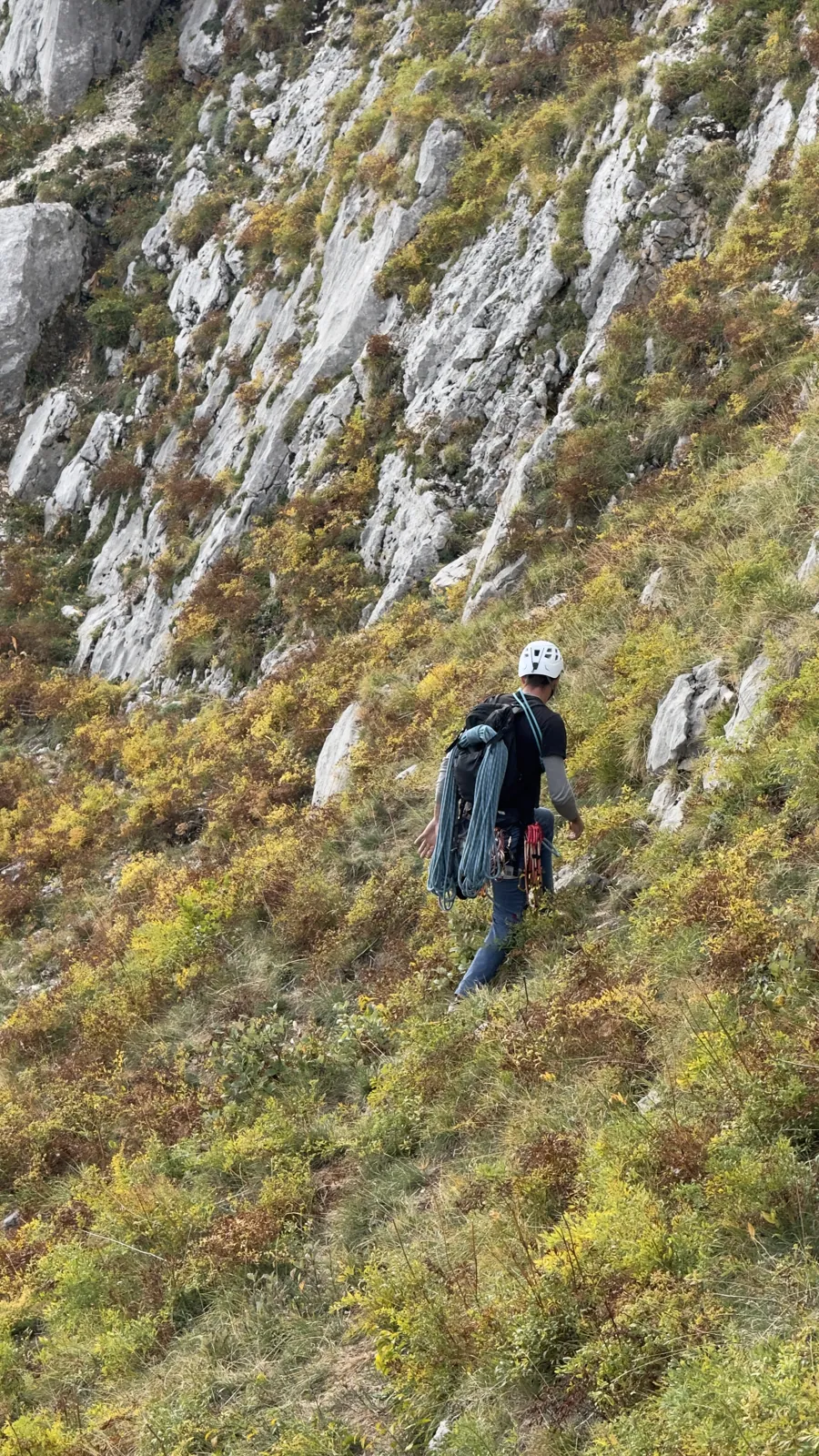 Grimpeur casqué, sac de corde au dos, dans une pente herbeuse raide