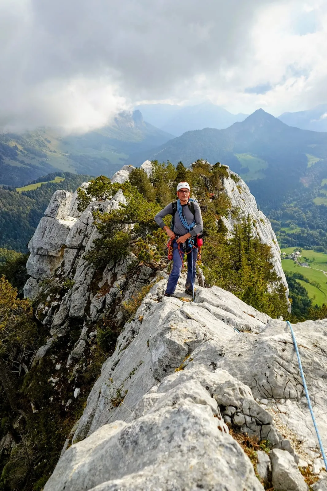 Grimpeuse debout au sommet d'une arête calcaire, montagnes et nuages derrière