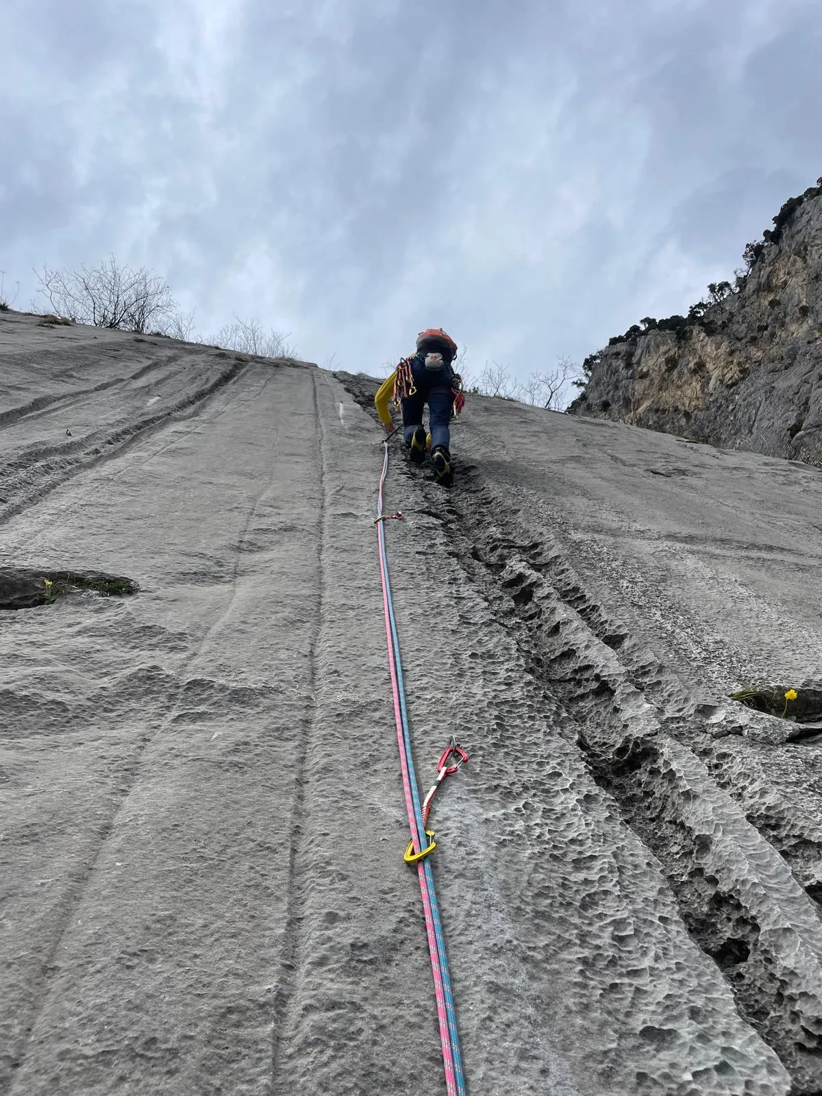 Grimpeur sur paroi calcaire grise vu d'en haut, vallée alpine au fond