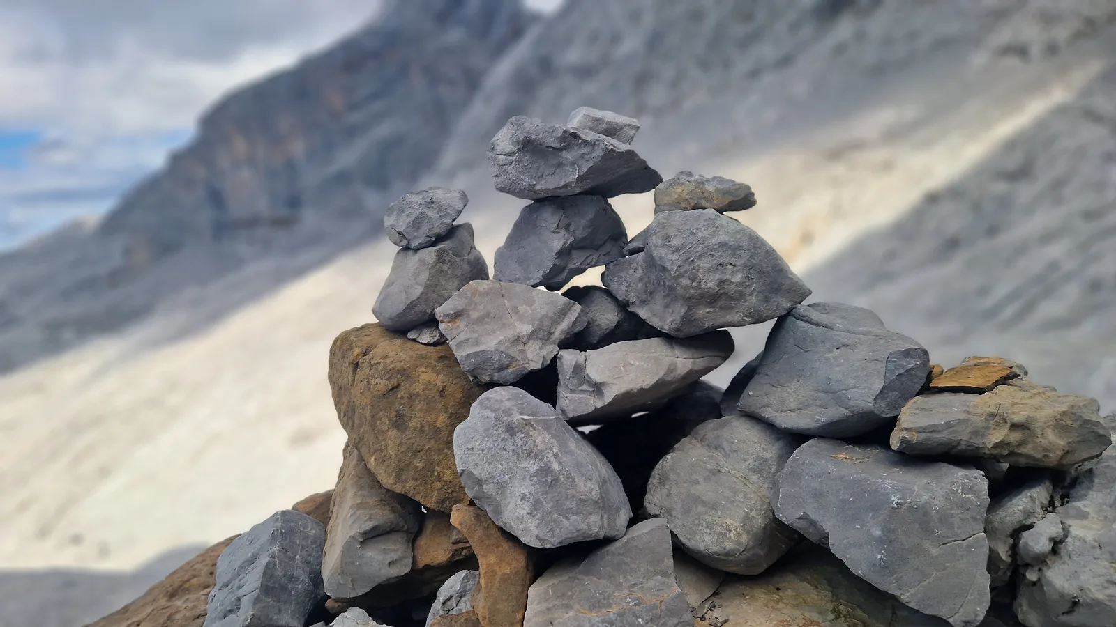 Grimpeur assis face à un cairn en sommet, vue panoramique