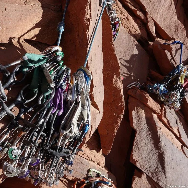 Rack de coinceurs mécaniques et de nuts alignés sur une fissure de grès rouge — la panoplie du grimpeur trad