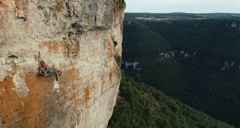 Vue aérienne d'une cordée en bivouac sur une vire calcaire, gorge boisée à 300 mètres en contrebas