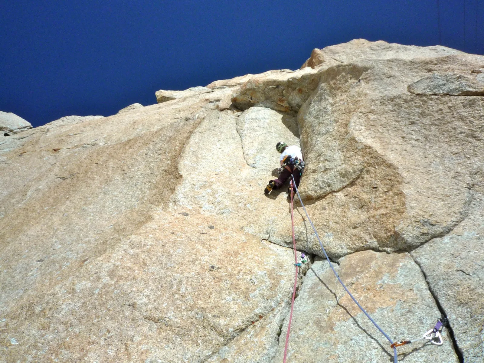 Grimpeur sous un surplomb de granite clair, cordes qui descendent le long de la dalle, ciel bleu