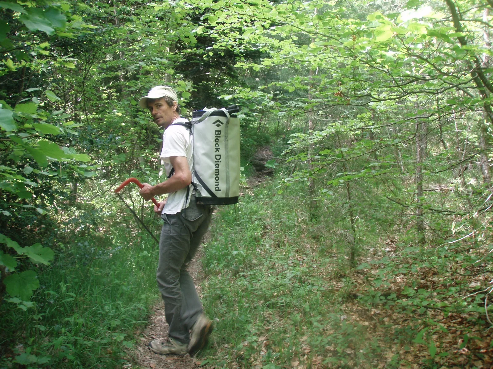 Grimpeur sur un sentier en sous-bois, un gros sac sur le dos, en route vers le pied des voies