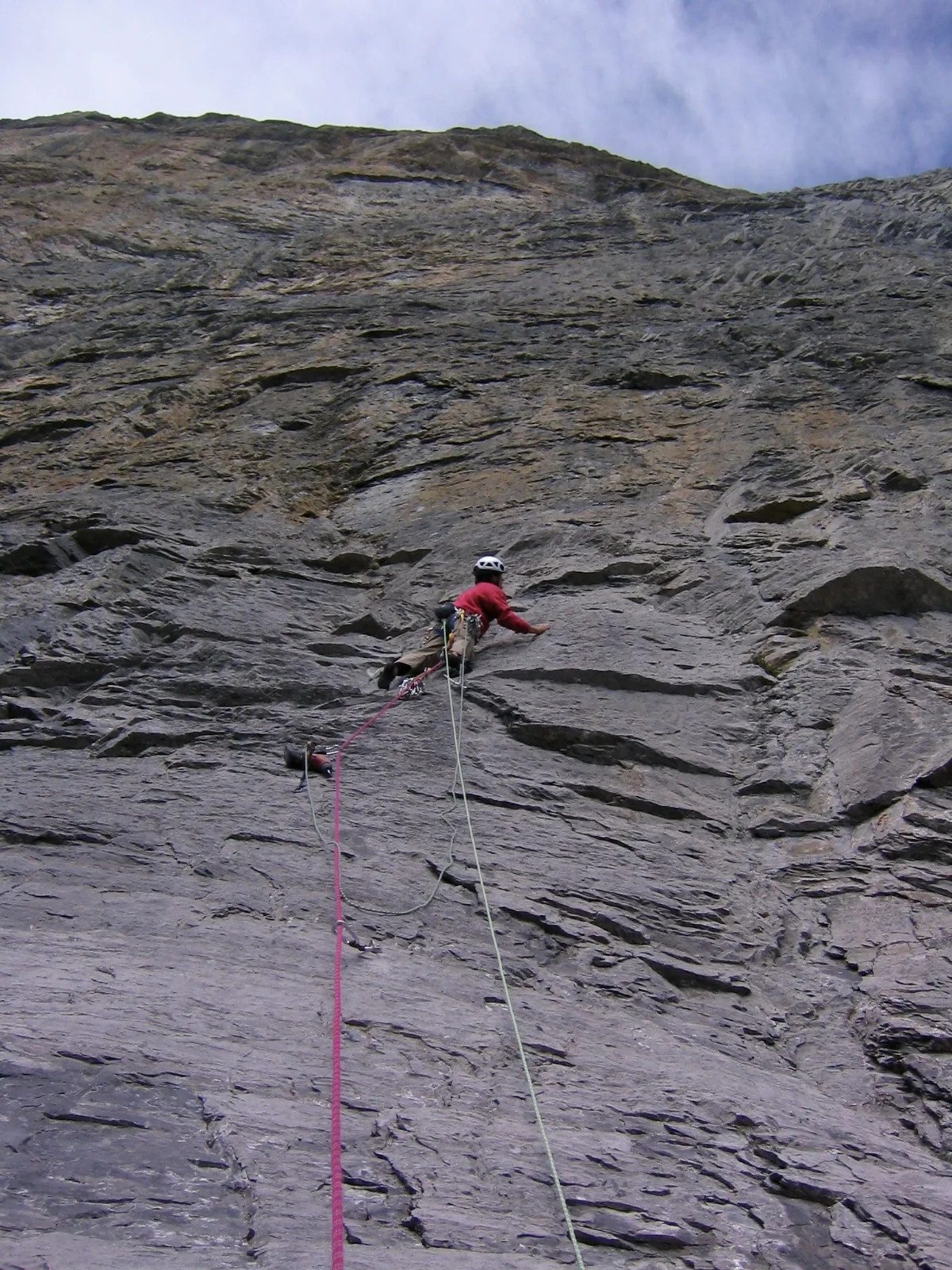 Grande paroi calcaire grise et verticale, un grimpeur au milieu du mur, deux cordes qui pendent jusqu'en bas