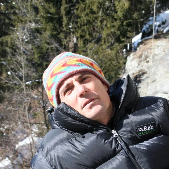 Portrait de Gilles Brunot, bonnet de laine et doudoune, au pied d'une falaise en hiver