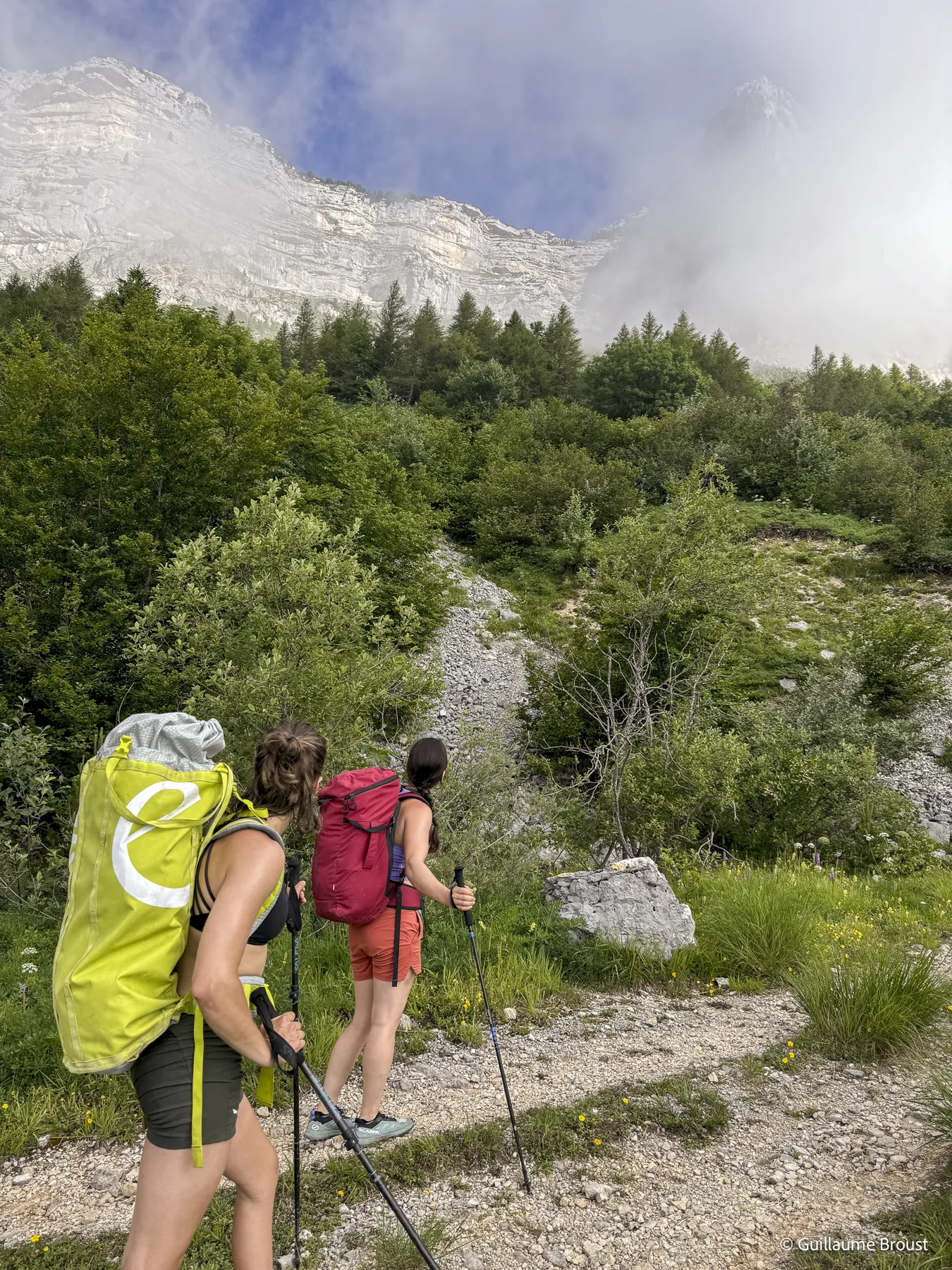 Deux grimpeuses sac au dos sur le sentier d'approche, paroi dans les nuages