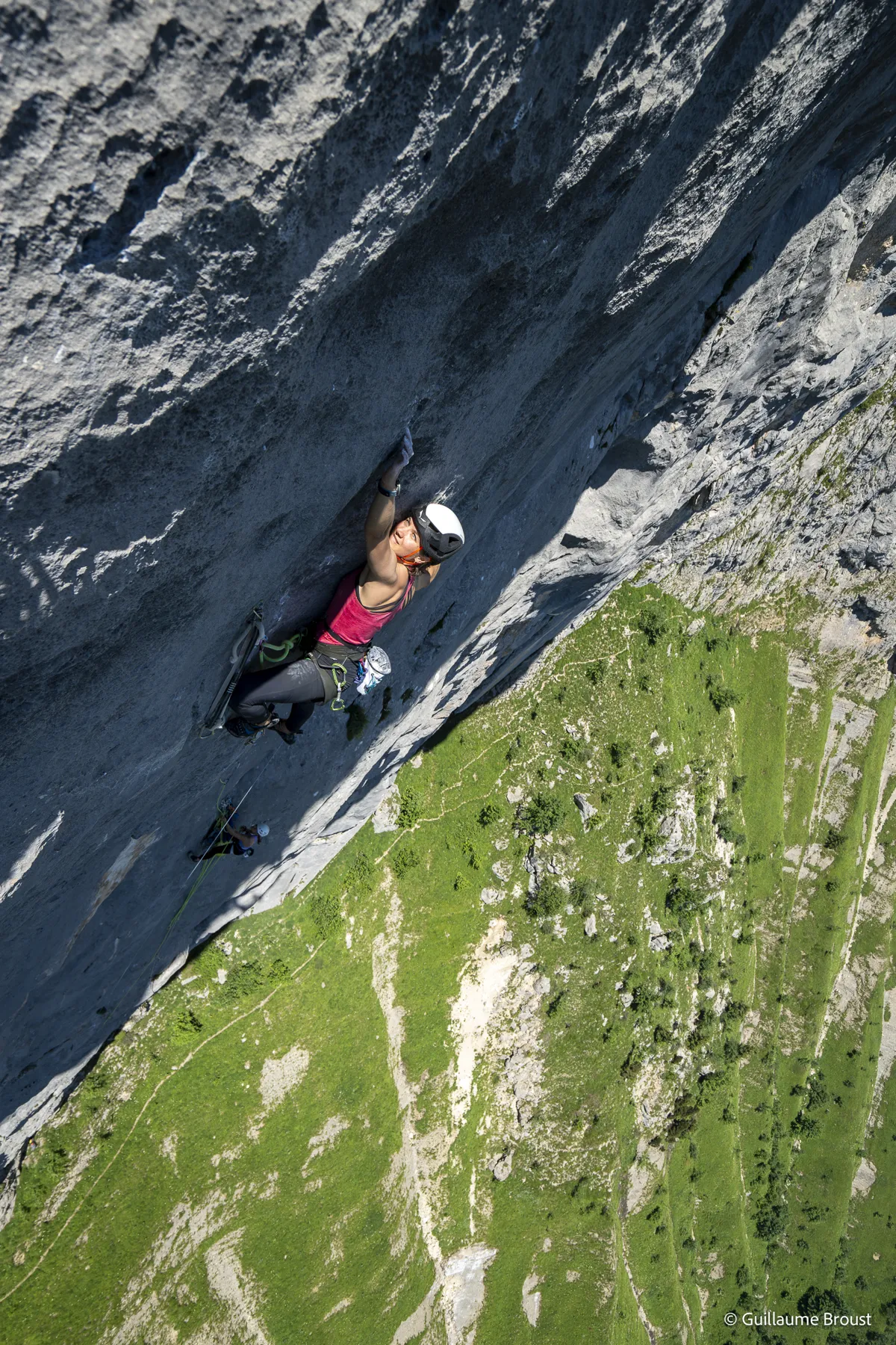 Vue plongeante sur une grimpeuse en tête, prairie très loin en contrebas