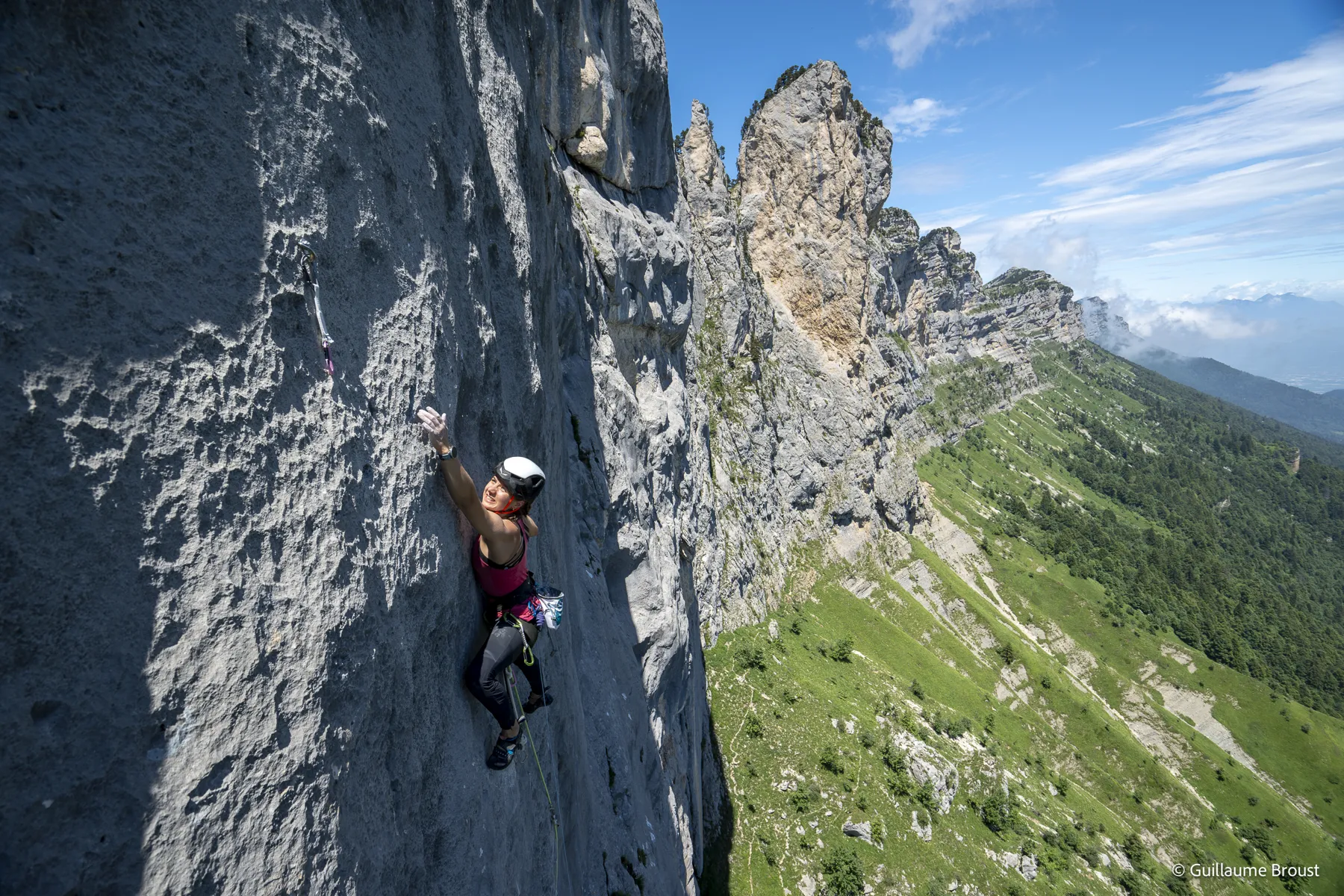 Grimpeuse en tête sur un mur calcaire gris, aiguilles rocheuses et vallée en contrebas